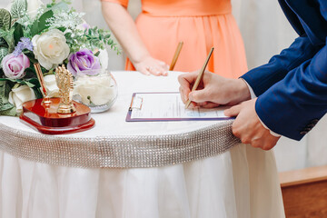young man standing at wedding ceremony and signing wedding documents, groom in blue costume, cropped, unrecognizable