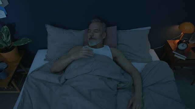 View from above of senior man having nightmare, suddenly waking up in bed and feeling anxious during night