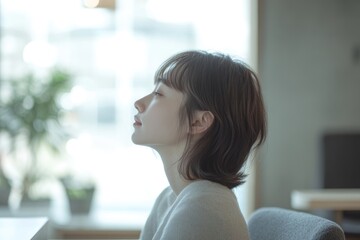 A young woman with short brown hair sits by a window, lost in thought, serene and peaceful.
