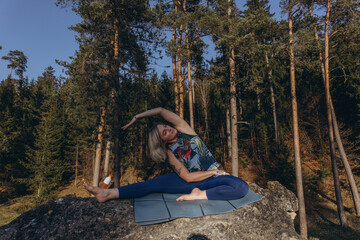 A woman meditating and practicing yoga on top of a rock at sunset, embracing wellness, mindfulness,...