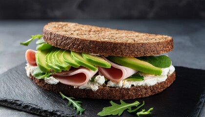 ham sandwich with cream cheese green salad avocado and rye bread on a black marble board dark grey background close up