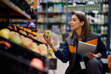 female grocery store worker using digital tablet at fresh fruit section.
