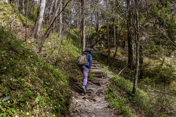 Obraz premium A young man in his thirties wearing a wide-brimmed hiking hat and clothes, with a backpack, walks along a picturesque alpine path, in spring in Austria