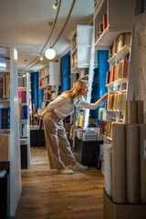 Enthusiastic woman selects books in bookstore alone. Female book lover browsing, searching...
