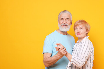 Lovely senior couple holding hands on orange background. Space for text