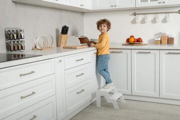 Little boy with cookies standing on step stool near countertop in kitchen