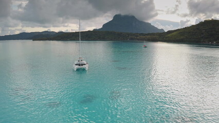 Bora Bora discovery and travel: white catamaran sailing in tranquil turquoise water with mount...