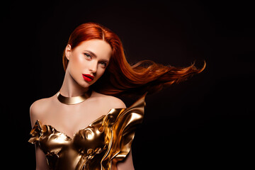 Stunning young woman in golden dress with red hair and captivating beauty posing gracefully
