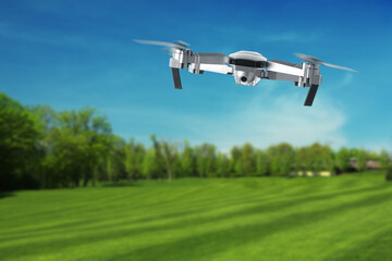 Drone with camera flying over green meadow. Unmanned aerial vehicle for surveillance