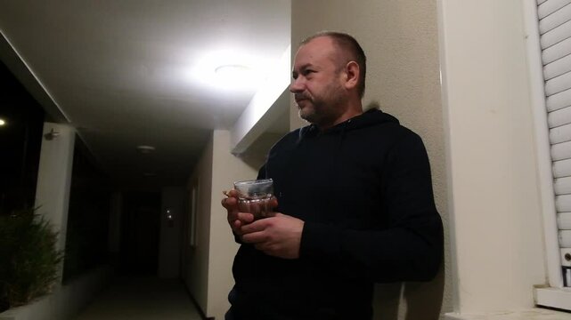 Man contemplating with drink and cigarette in dimly lit corridor setting