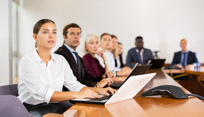 Young caucasian woman sitting at desk in meeting room and using laptop duting conference..