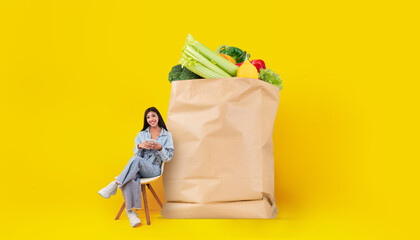 A customer sits comfortably beside a large paper bag filled with fresh vegetables and fruits,...