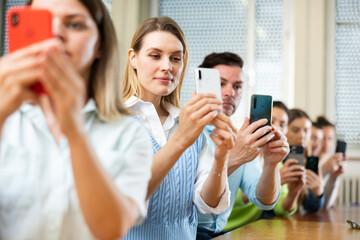 Fellow students sitting at their desks in the university auditorium are taking photo with smartphone cameras