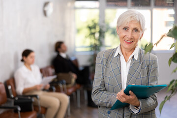 Interested positive elderly businesswoman holding folder with papers, writing tasks and...
