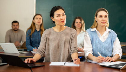 Students writing in notebook and typing on laptop during class in university classroom