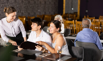 Adult female waiter in uniform takes order from young couple in restaurant