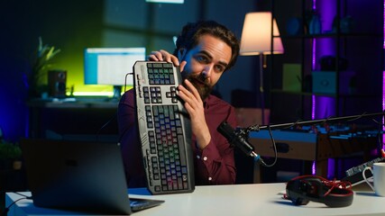 Man in studio reviewing gaming keyboard received from sponsoring brand. Online show host paid to...