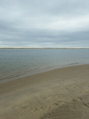  Curved Sandy Shoreline with Calm Water and Distant Dunes Under Overcast Sky