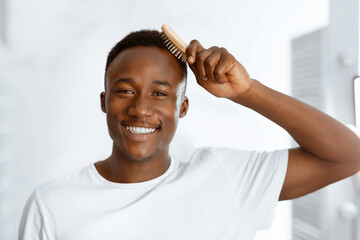 Male Haircare. Handsome Black Man Combing And Brushing Short Hair With Brush Smiling Looking At...