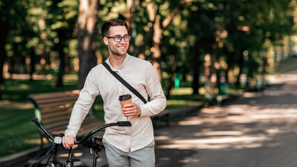 A young man stands next to his bike on a tree-lined street, smiling as he holds a coffee cup. The atmosphere reflects a relaxed lifestyle, typical of urban millennials enjoying their day, copy space