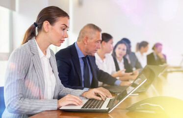 Woman sitting at table beside her colleagues during meeting in conference room and using laptop.