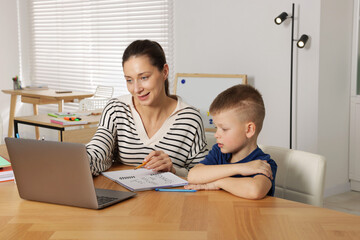Cute boy and teacher with laptop at desk in school