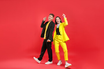 Naklejka premium Happy couple in stylish clothes dancing on red background