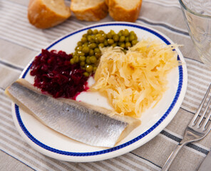 Canned peas with sliced beets, herring and cabbage on a plate side view.