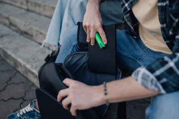 Student putting tablet and highlighter in backpack on university steps