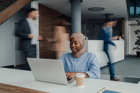Focused black muslim woman working on laptop in busy office