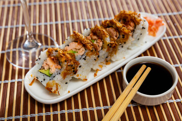 Appetizing Sake Cooked Roll sushi inspired by Japanese cuisine with baked salmon and soft avocado, sprinkled with crispy fried onion traditionally served with soy sauce, wasabi, and gari..