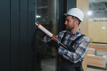 A worker is applying polyurethane foam to fill gap between sash and window frame in prefabricated...