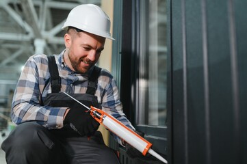 A worker is applying polyurethane foam to fill gap between sash and window frame in prefabricated...