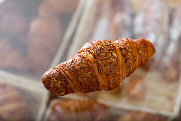 Croissant with whole wheat seeds on the counter in the bakery. Pastry with sesame seeds and flax seeds close-up. Whole grain bun for breakfast