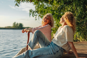 Mother and daughter relaxing by the lake, enjoying golden hour light