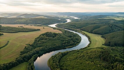 An aerial view of a winding river flowing through a lush green landscape of forests and fields under a hazy sky, symbolizing nature, environment, journey, flow, wilderness, natural beauty