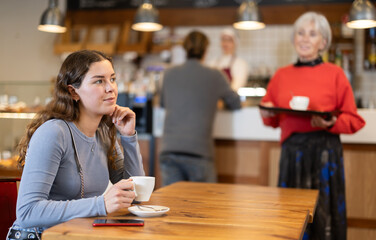 Food court girl visitor sits near table, drinks coffee and spends time in public place. Bored client spend time at cafe hall