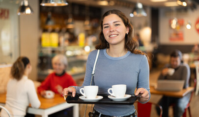 Girl visitor in self-service cafeteria carries tray with two cups of coffee. Customer has purchased...