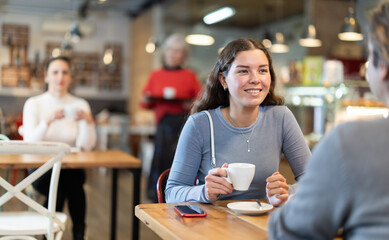 During lunch break, girl at cafe drinking coffee, talks with boyfriend, spends time in company of friend. Meeting on neutral territory, discussing personal and business issues