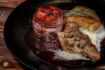 Luxurious Dish: Round Steak with Mushrooms and Potato on Black Plate, on Wooden Table, for Restaurant Menu and Advertising Materials, Side View.