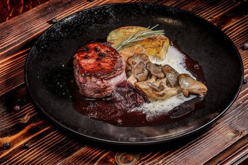 Refined Gourmet Steak with Accoutrements on an Elegant Black Plate, Artfully Placed on a Wooden Table, Emphasizing Culinary Artistry and Elegance.
