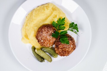Traditional Cutlets with Mashed Potatoes and Gherkins on White Plate, Garnished with Parsley, Top View, for Cafe Menu and Home Cooking Advertising.