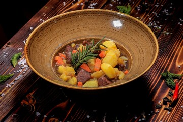 Aromatic rustic goulash with potatoes and carrots, close-up, dark background