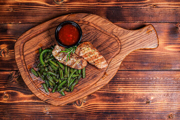 Image 1: Overhead View of Grilled Meat with Green Beans and Red Sauce on Dublin Wooden Board, Dark...
