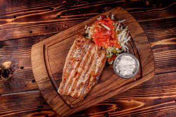 Healthy grilled fish fillet with side on rustic board, top view on dark background.