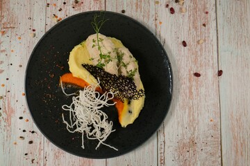 Elegant poultry dish with mash and vibrant sauce on dark plate, top view on light wood.