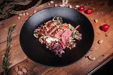 Hearty Warm Salad with Roast Beef, Pine Nuts and Fresh Vegetables, Artfully Served on Black Plate...