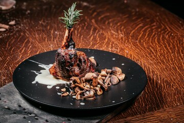 Appetizing Lamb Shank with Mushrooms on Black Plate, with Rosemary Garnish and Sauce on Wooden Table, Gastronomic Presentation of Haute Cuisine.