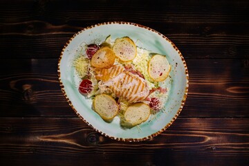 Appetizing Chicken Caesar Salad with Grilled Chicken on Handmade Plate, with Croutons and Tomatoes on Wooden Table, Top View, Culinary Concept for Restaurant.
