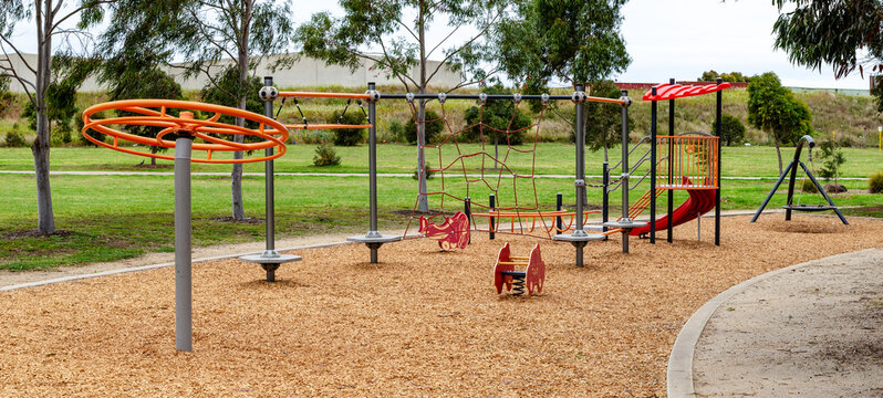 Panoramic view of a modern children's playground with various play structures set on a wood chip surface for safety, surrounded by eucalyptus trees providing natural shade, in Australia.
